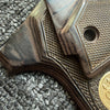 Close-up of a dark wood custom diamond pattern grip for a firearm resting on a gray textured surface.