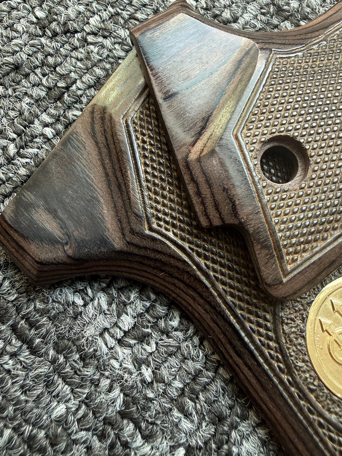 Close-up of a dark wood custom diamond pattern grip for a firearm resting on a gray textured surface.