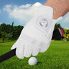 A hand wearing a white breathable golf glove is shown hitting a golf ball on a green lawn.