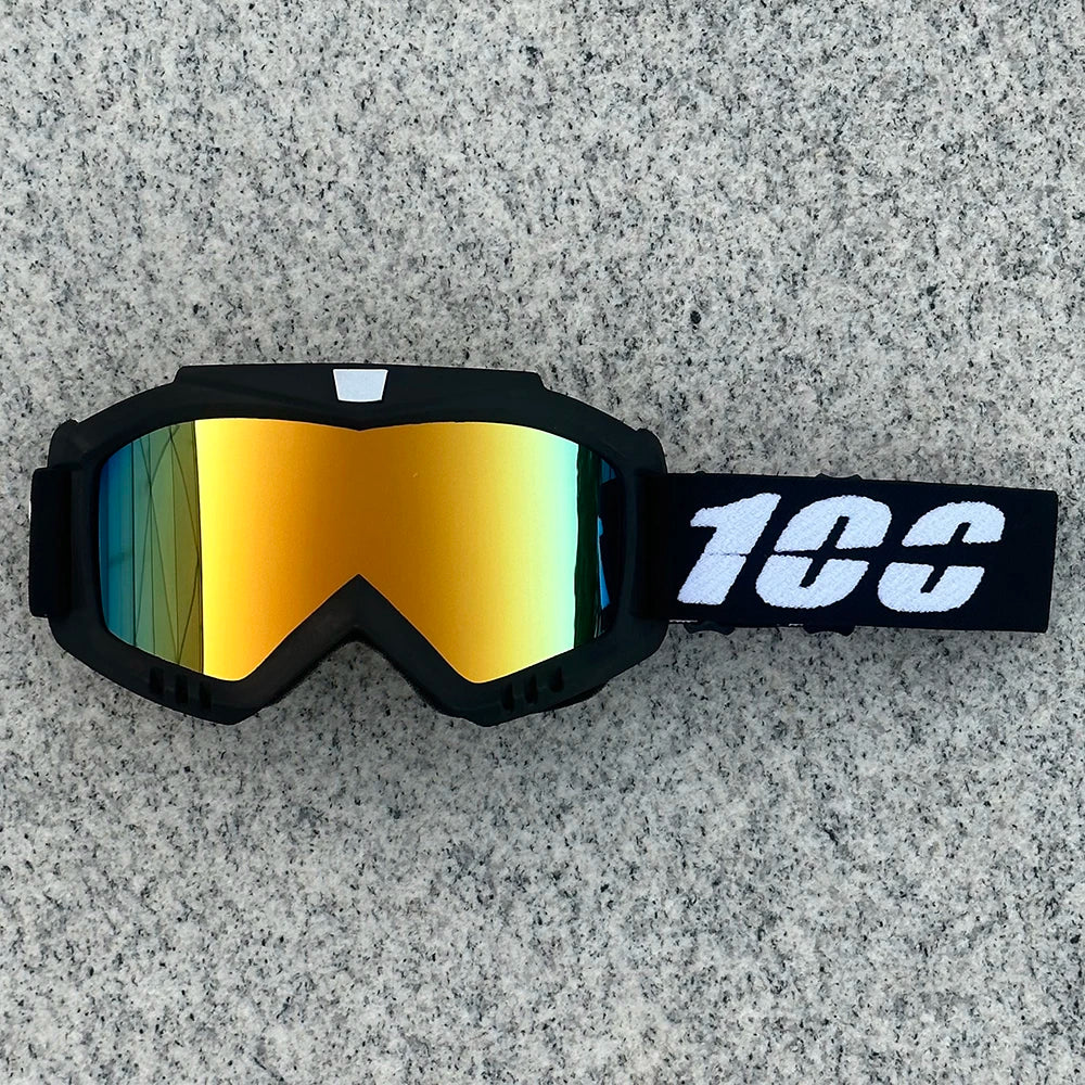 A pair of black goggles with orange-tinted lenses and a white '100' logo on the strap, resting on a gray surface.