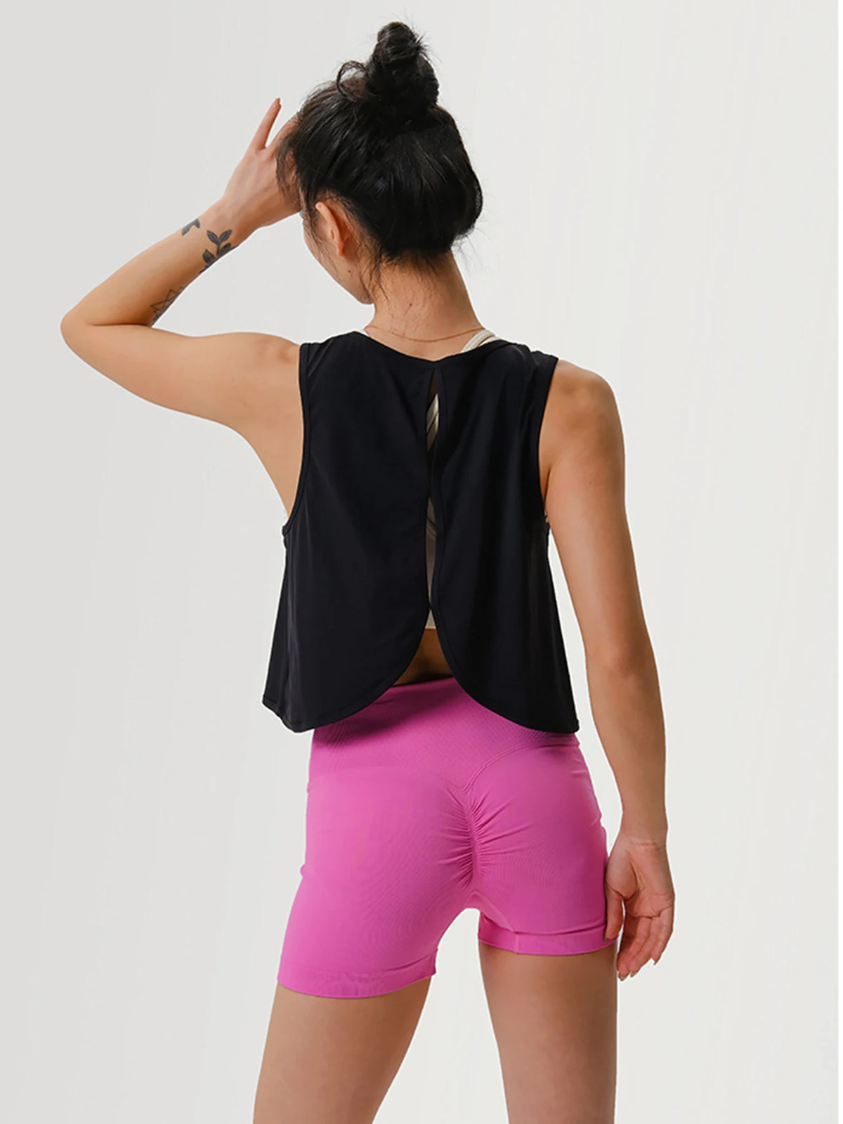 Eine Frau trägt ein schwarzes, nahtloses Crop-Top und leuchtend pinke Sportshorts.
