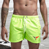 A muscular man wearing neon yellow quick-drying swim shorts standing near the ocean.