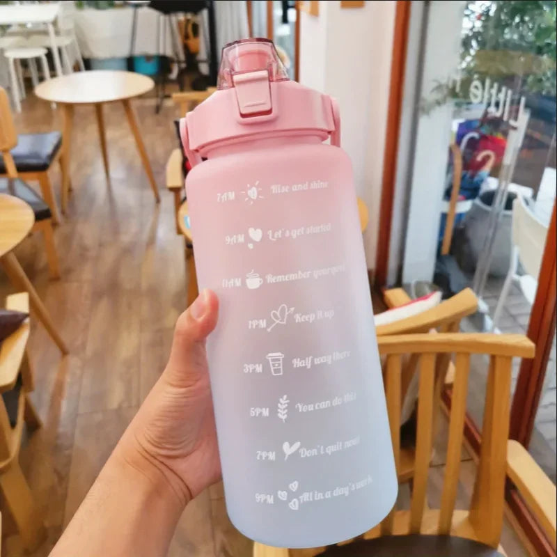 Una mano sostiene una botella de agua deportiva rosa con una pajita contra un fondo interior desenfocado.