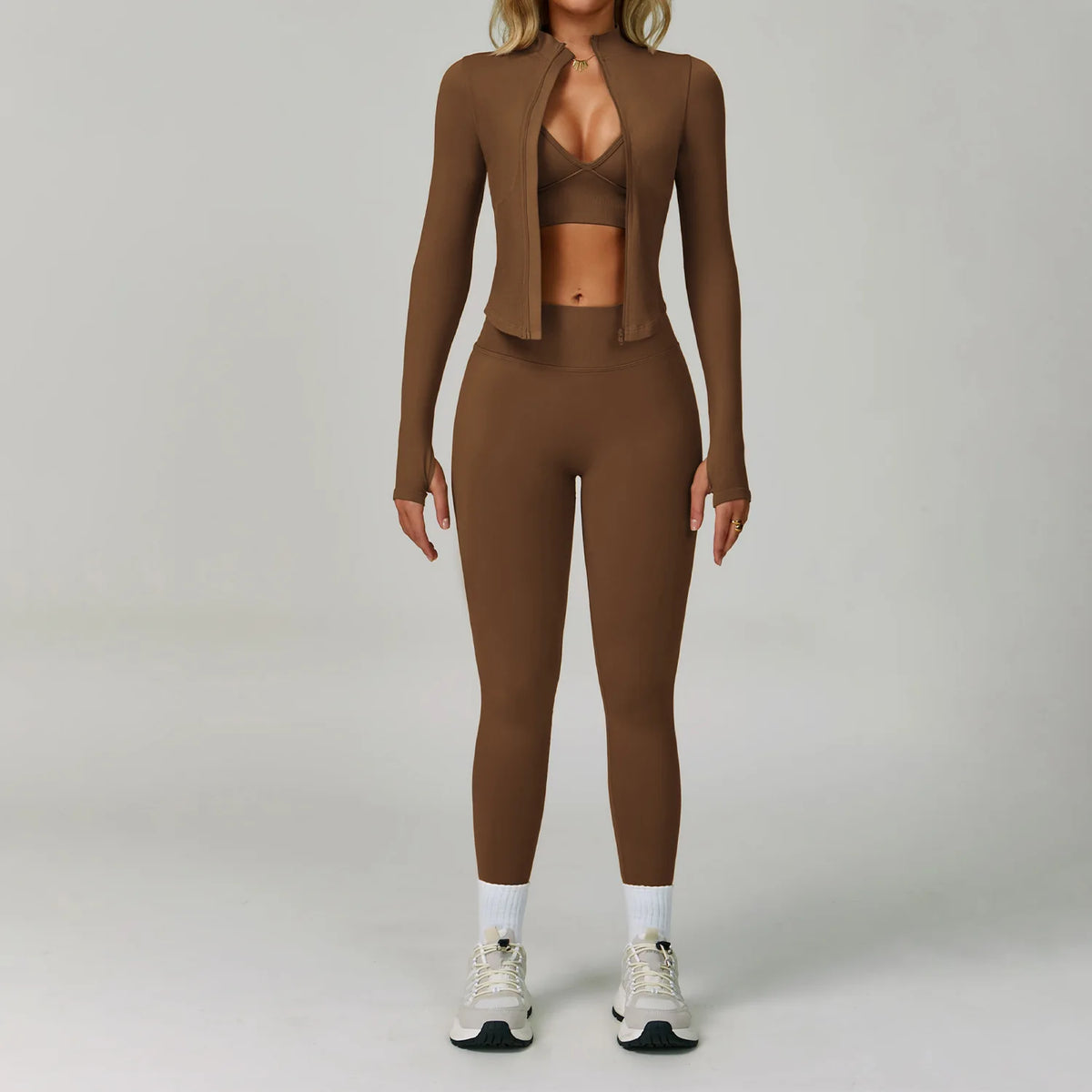 Eine Frau modelliert ein nahtloses Sport-Yoga-Set in Braun mit einem Cropped-Jackett und passenden Leggings.