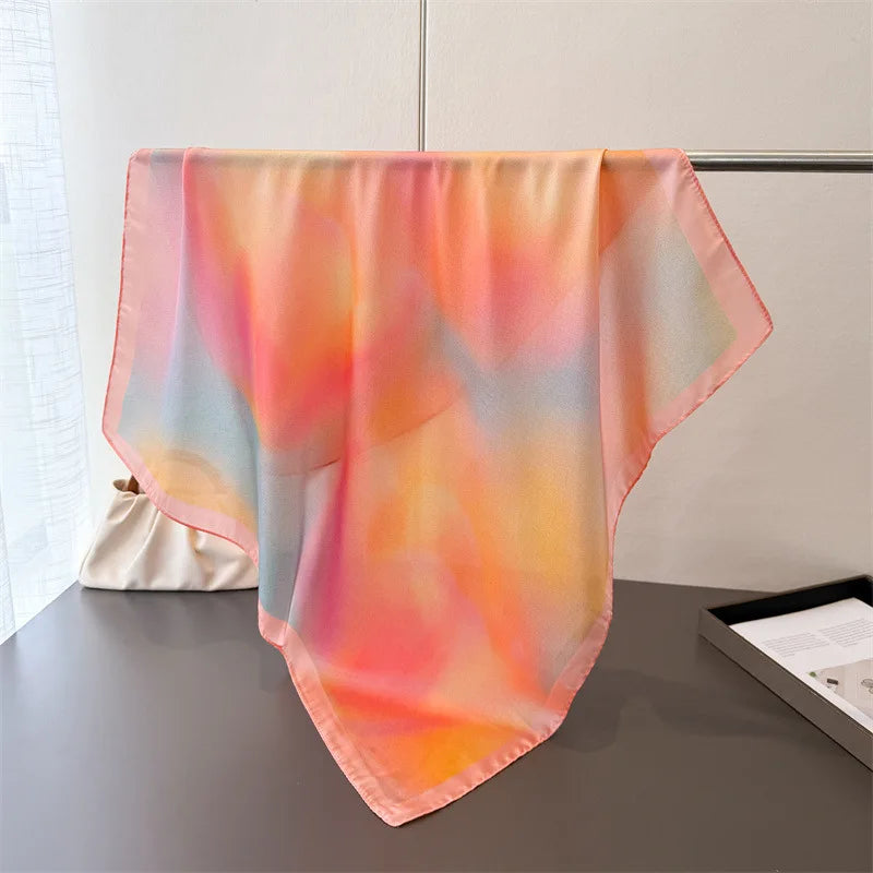 A sheer silk-touch floral hair scarf in soft pink and orange hues draped on a dark surface.