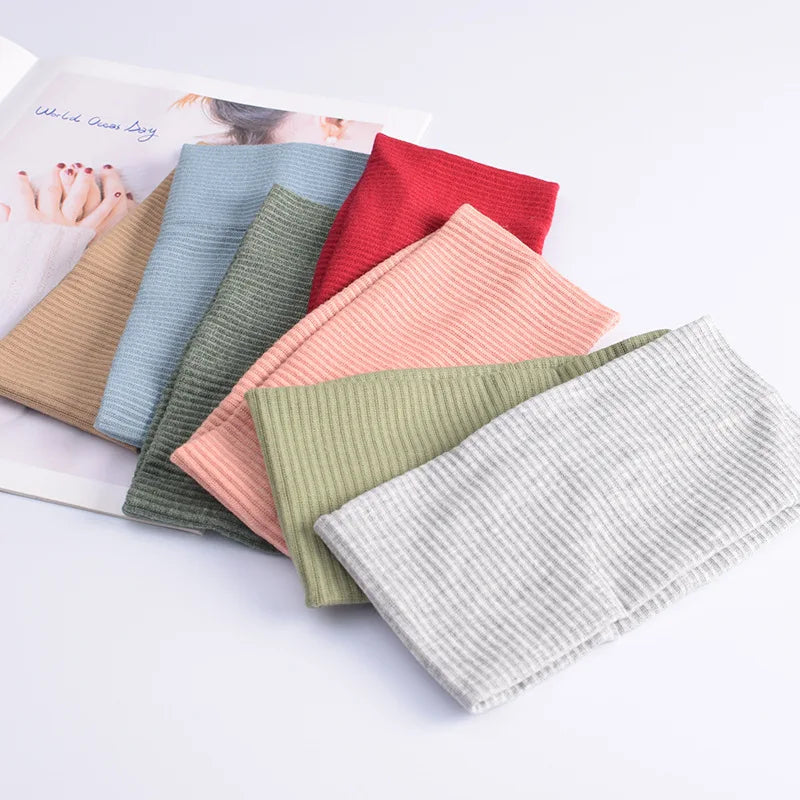 A collection of soft cotton knitted headbands in various pastel and earthy tones are displayed on a white surface.
