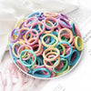 A pile of 50 mixed color elastic hair bands in various shades of pink, blue, and yellow on a white surface.