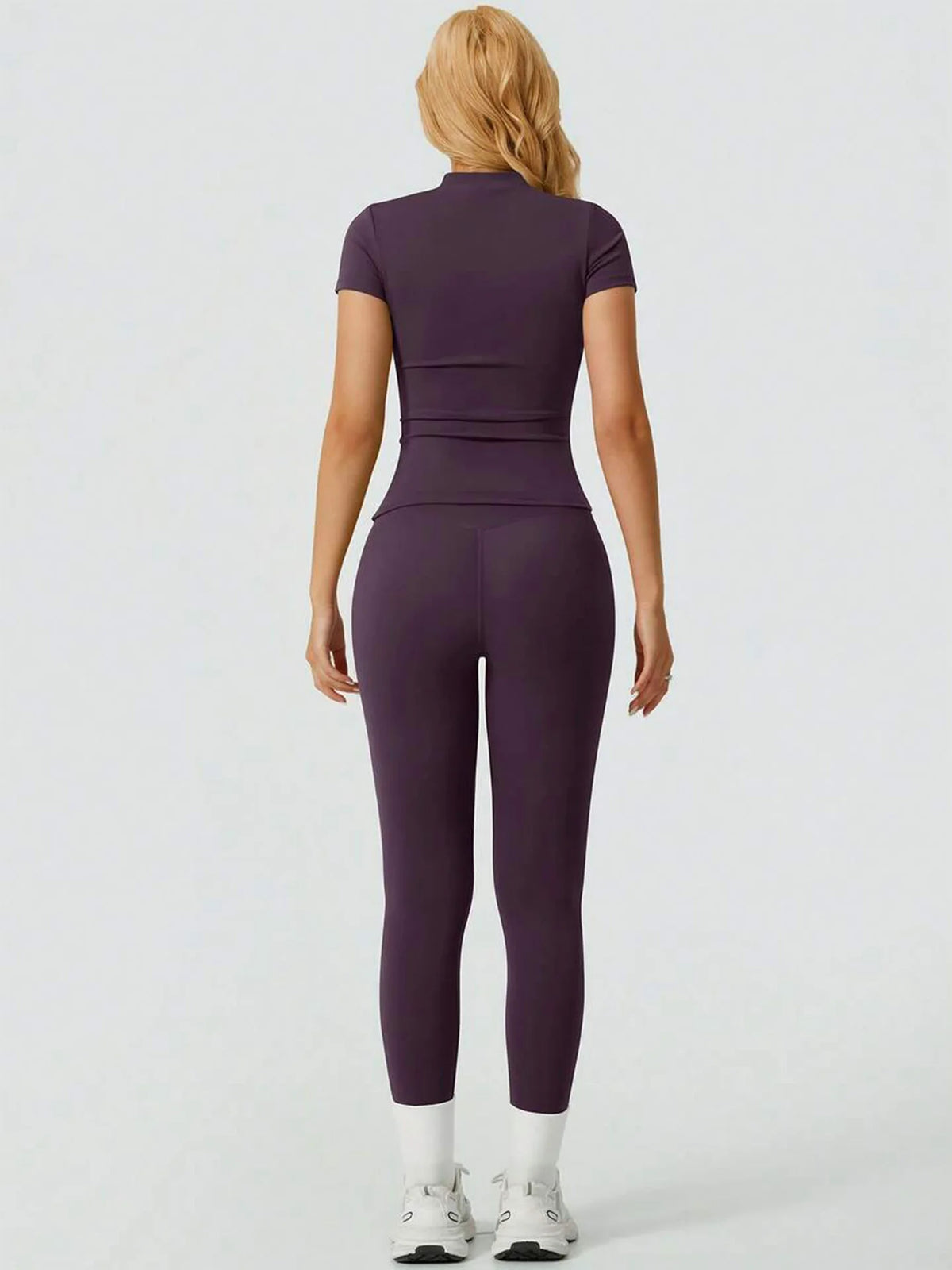 Eine Frau trägt ein lila Zweiteiler-Yoga-Set mit hohen Leggings und einem kurzärmeligen Oberteil.