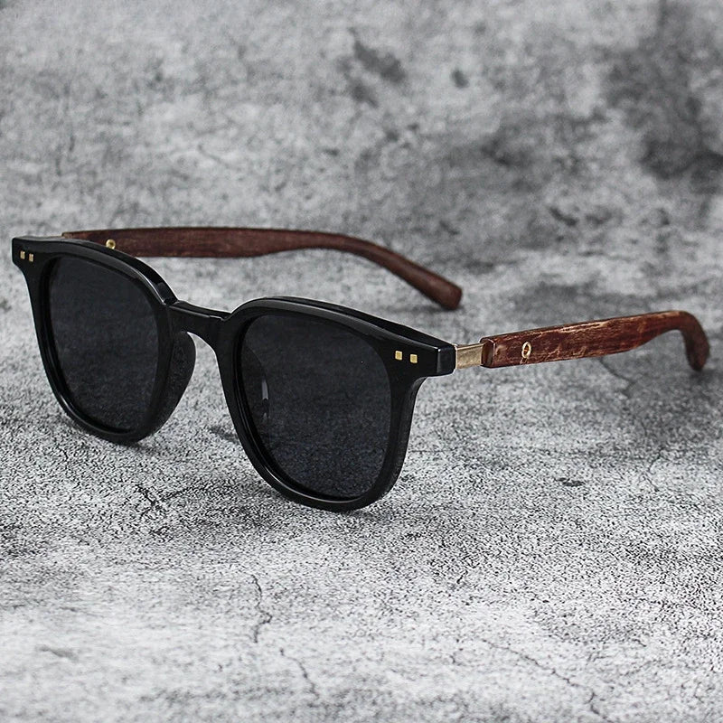 Black sunglasses with dark lenses and a brown wood grain frame resting on a gray textured surface.