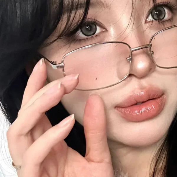 Close-up photo of a woman wearing retro square frame eyeglasses with light pink skin and dark hair.