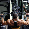 A muscular man lifts a barbell with wrist wraps in a gym setting.