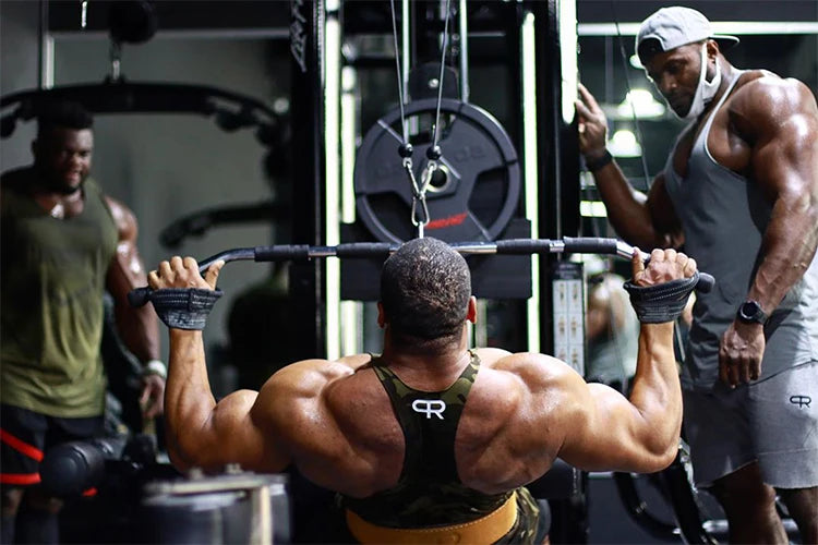 A muscular man lifts a barbell with wrist wraps in a gym setting.