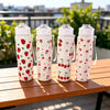 Four white tumblers decorated with red strawberries, cherries, and small flowers sitting on a wooden table.