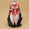 A satin square scarf featuring a red, white, and black geometric pattern tied around dark hair.