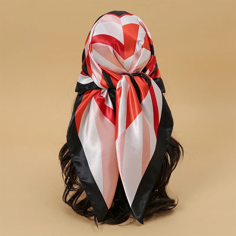 A satin square scarf featuring a red, white, and black geometric pattern tied around dark hair.