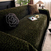 A dark green plush sofa cover blanket with a leopard print pattern, featuring decorative pillows and a small tray.