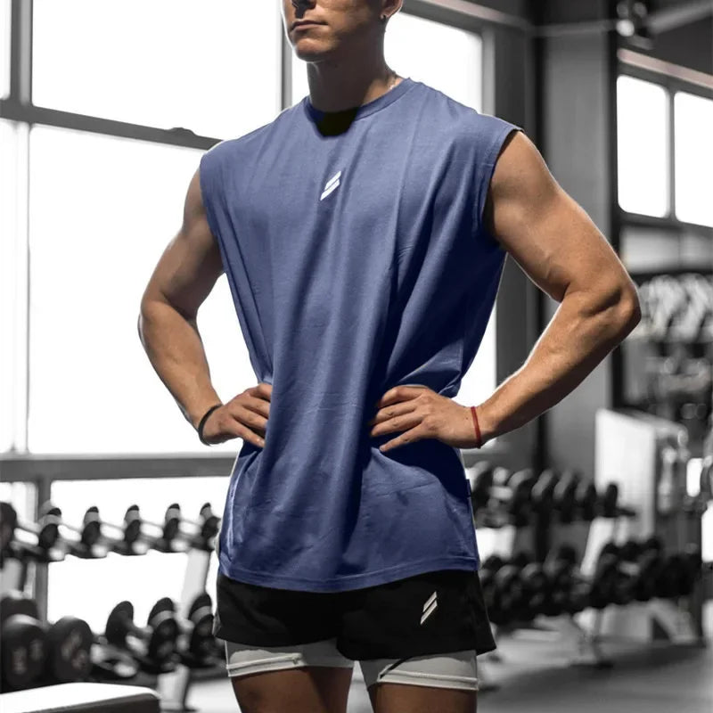 Mann in blauem, schnelltrocknendem Fitness-Tanktop und schwarzen Shorts in einer Sporthalle.