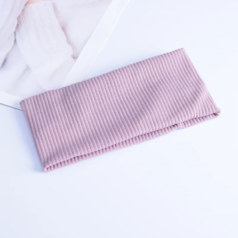 A light pink ribbed knitted headband lying on a white surface next to a white fabric.