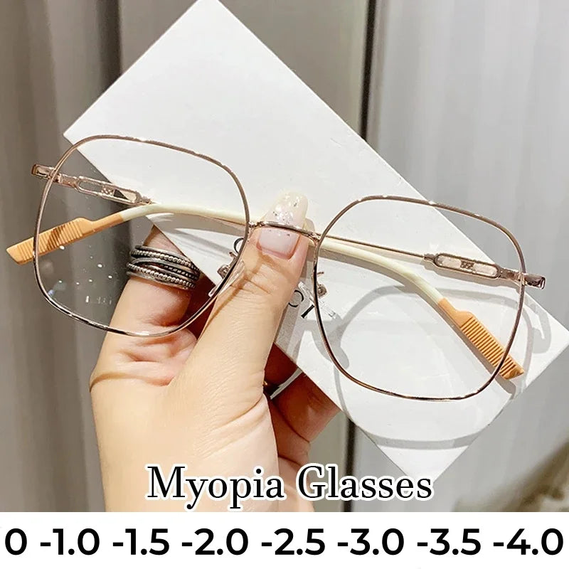 A hand holds a pair of thin, wire-framed reading glasses with light brown frames and white temples against a white background