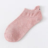Un par de calcetines de tobillo color rosa empolvado con una sutil textura de punto y un pequeño detalle bordado de cara sonr
