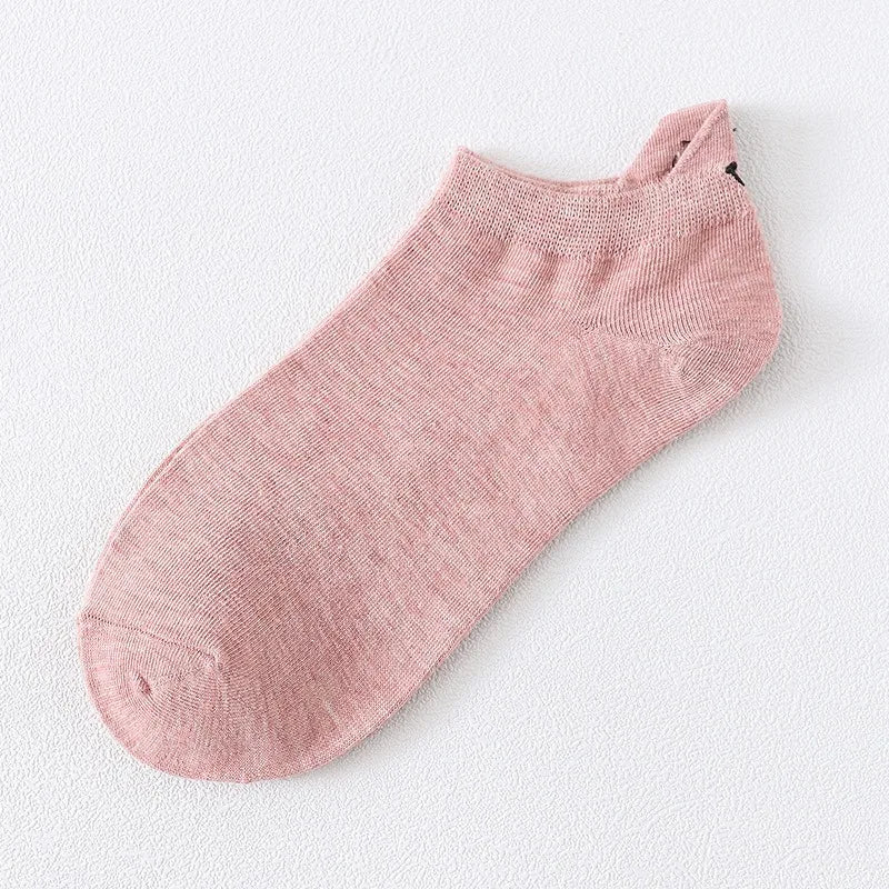 Un par de calcetines de tobillo color rosa empolvado con una sutil textura de punto y un pequeño detalle bordado de cara sonr