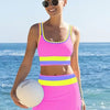 A woman wearing a color-block zigzag three-piece swimsuit set stands by the ocean.