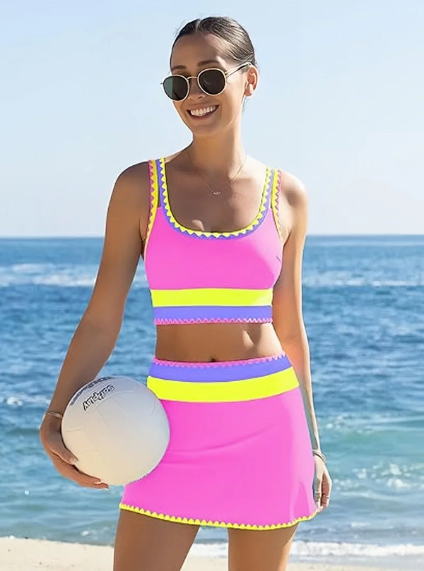 A woman wearing a color-block zigzag three-piece swimsuit set stands by the ocean.