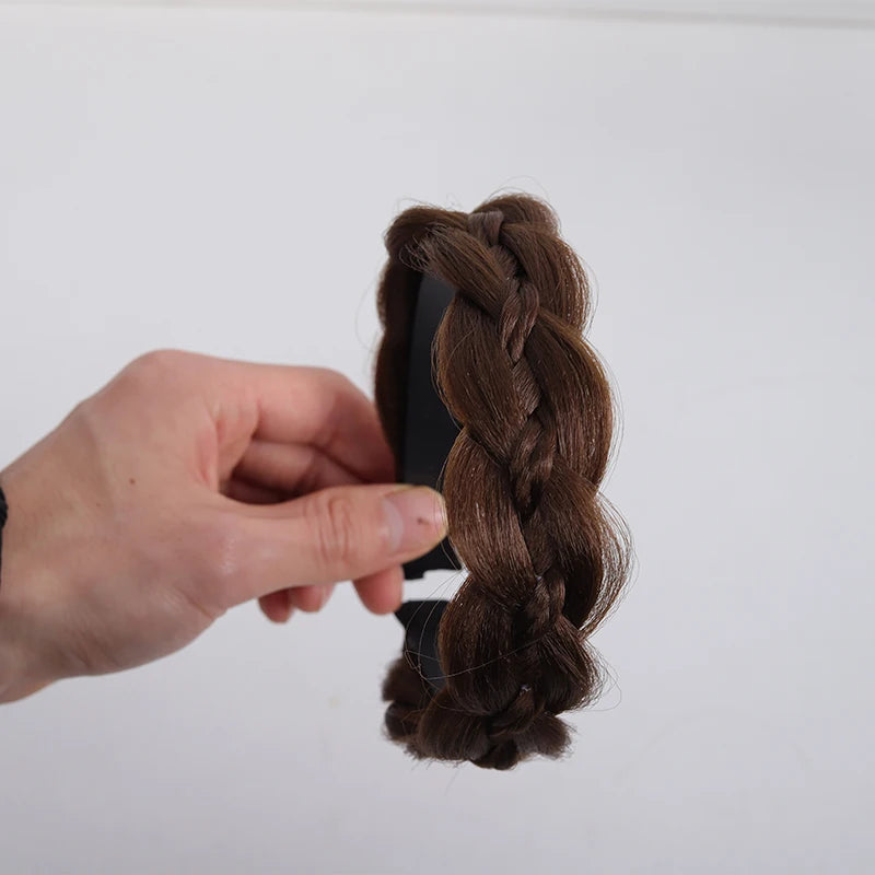 A hand is holding a dark brown twisted braided wig headband against a white background.