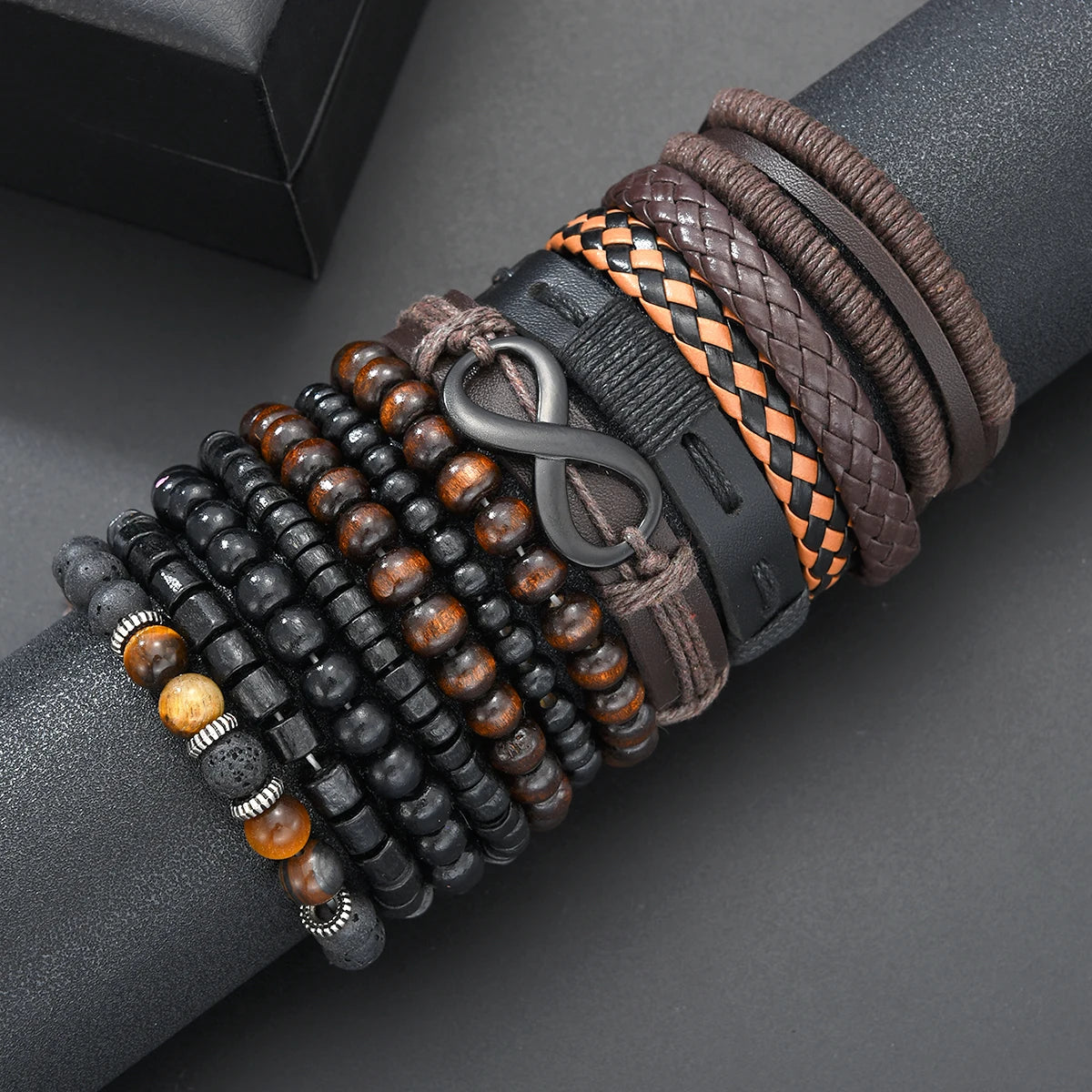 A close-up of various brown, black, and orange beaded leather bracelets stacked on a dark gray wrist.