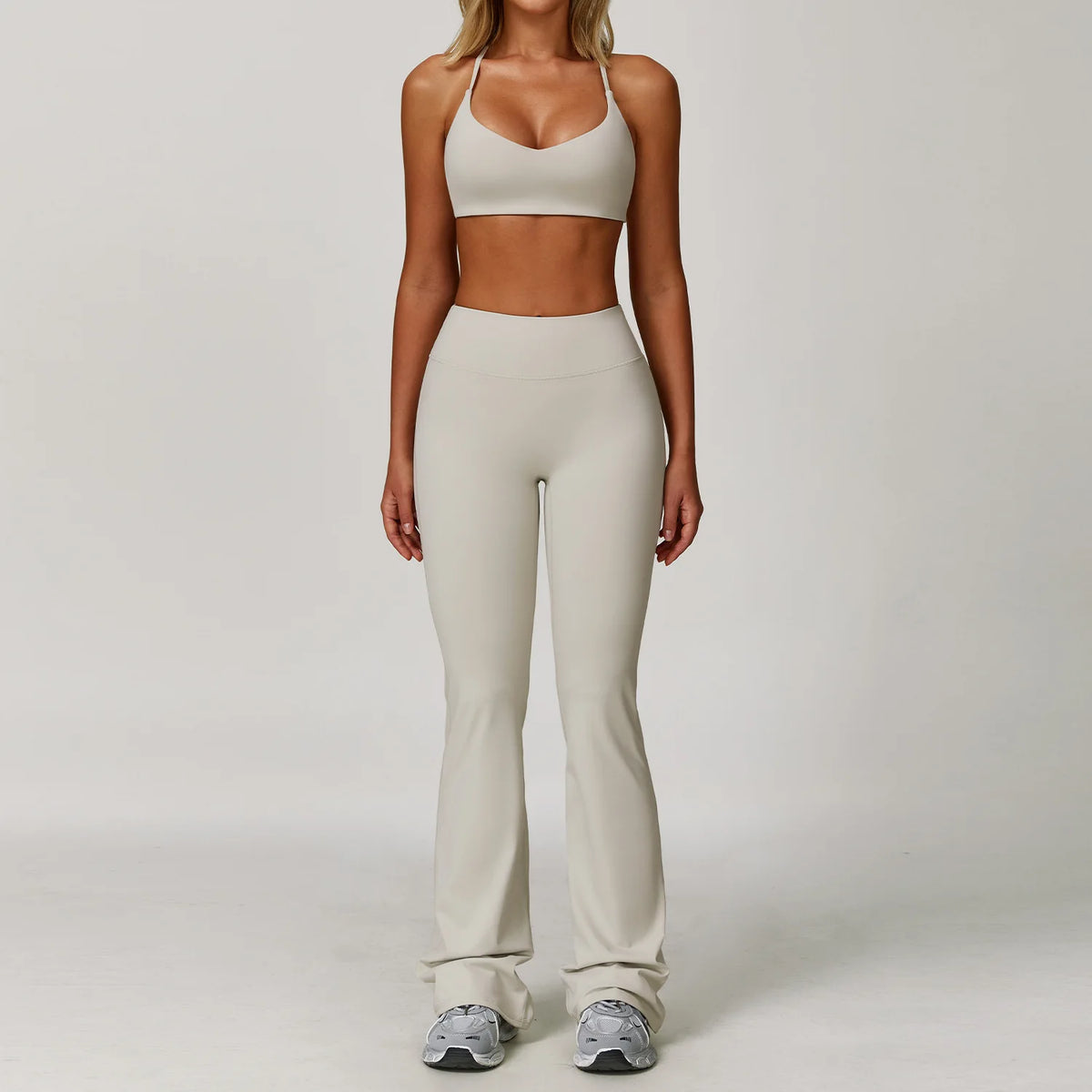 A woman models a beige 3-piece yoga sports set consisting of a cropped top, leggings, and a matching sports bra.