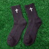 A pair of black knit mid-calf sports socks with white crosses lying on green grass.