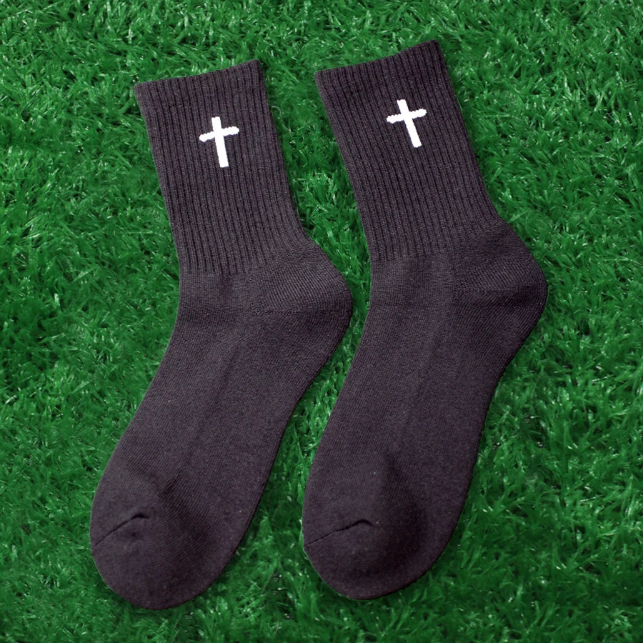 A pair of black knit mid-calf sports socks with white crosses lying on green grass.