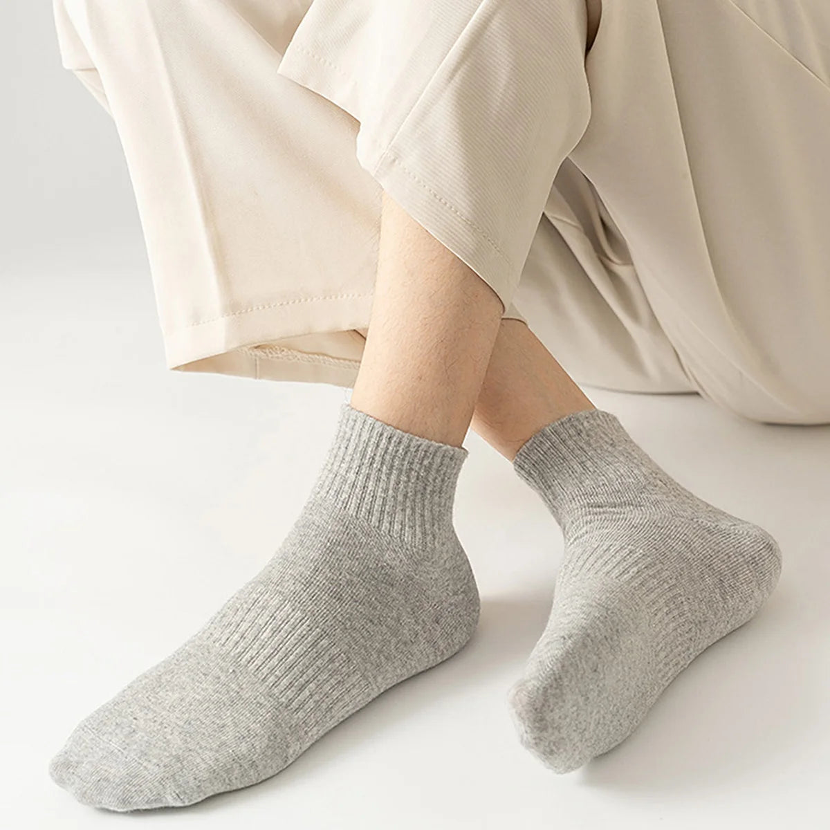 A pair of light gray premium athletic crew socks being worn by a person in beige pants.