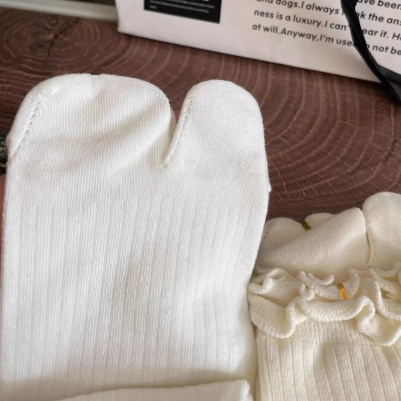 White knit crew socks with ruffled cuffs shown on a wooden surface.