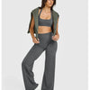 A woman models high waisted wide leg yoga pants in gray paired with a green open shirt.