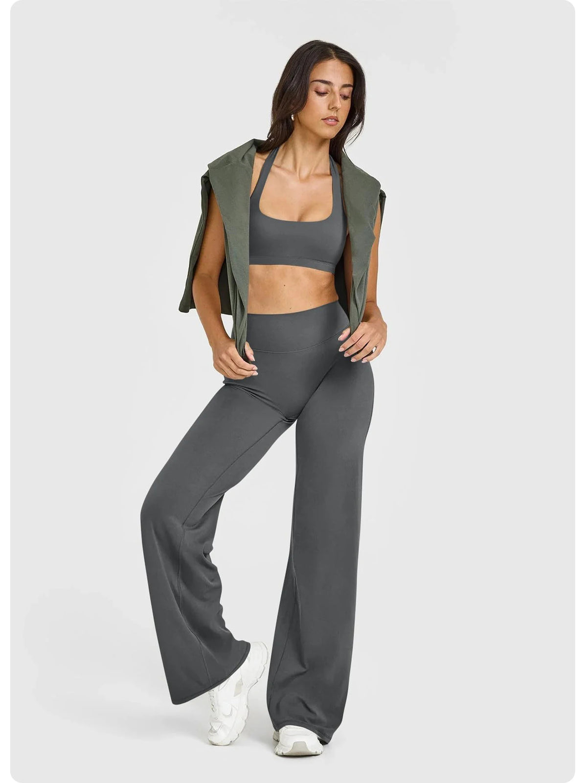 A woman models high waisted wide leg yoga pants in gray paired with a green open shirt.