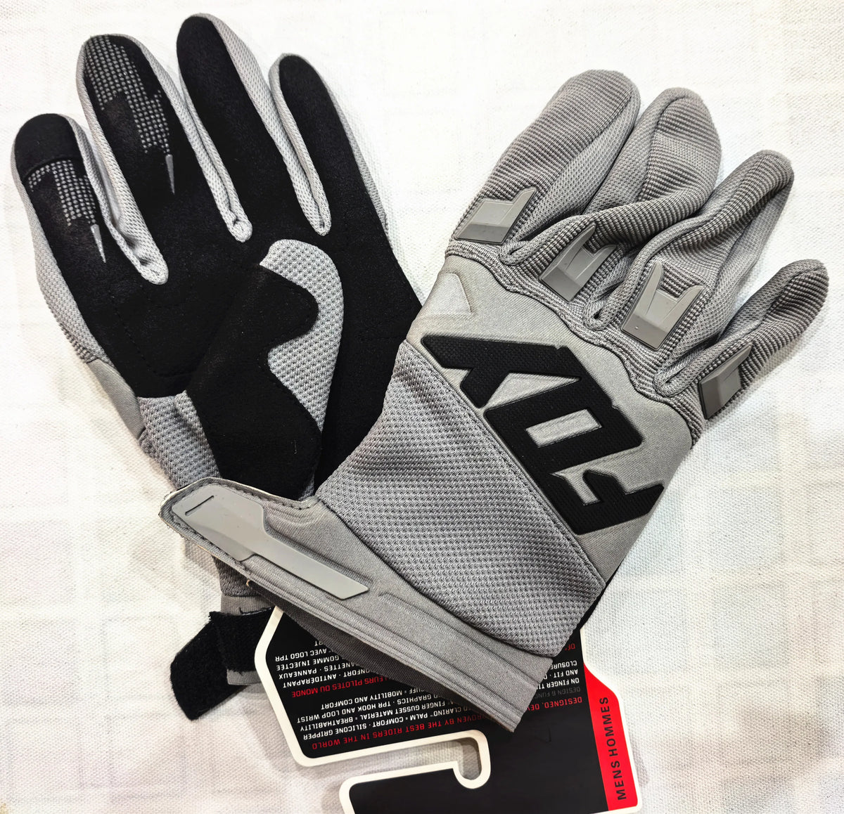A pair of gray and black durable motorcycle off-road riding gloves are displayed on a white surface.