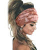 Una mujer vistiendo un pañuelo de estilo bohemio tie-dye color rosa polvoriento recogido en una coleta alta.