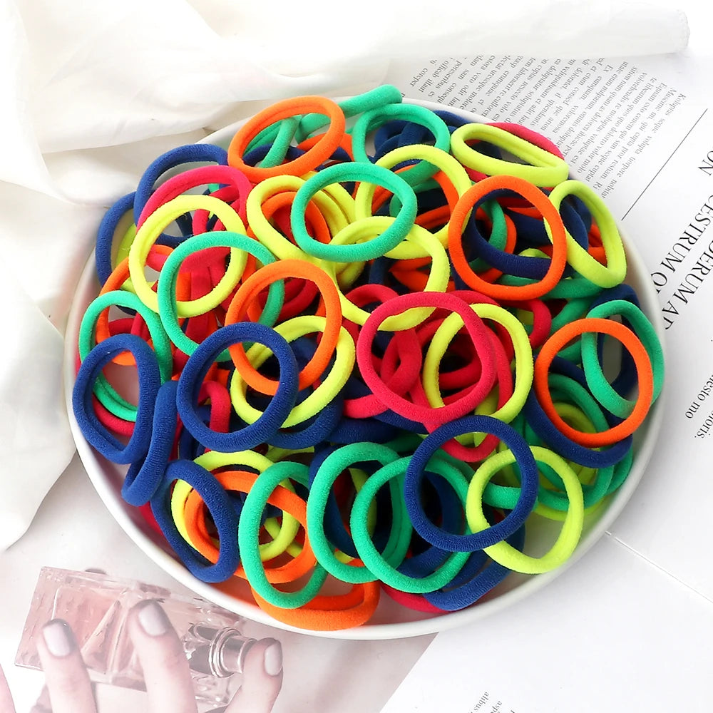 A pile of 50 pieces of mixed color elastic hair bands in various bright colors on a white plate.