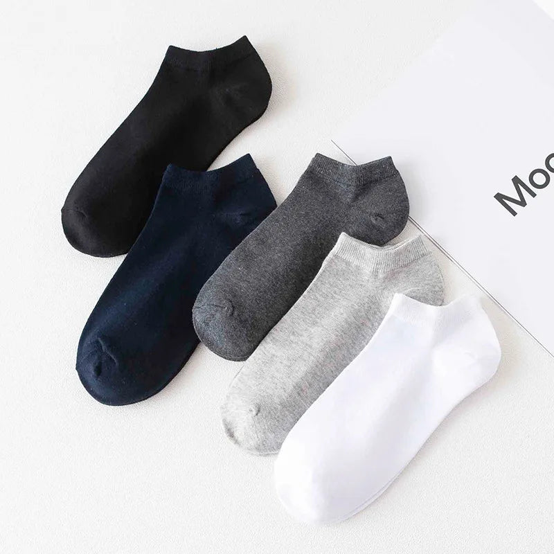 A collection of five ankle socks in black, navy blue, charcoal gray, light gray, and white laid out on a white surface.