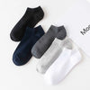 A collection of five soft lightweight ankle socks in black, navy blue, charcoal gray, light gray, and white laid out on a whi