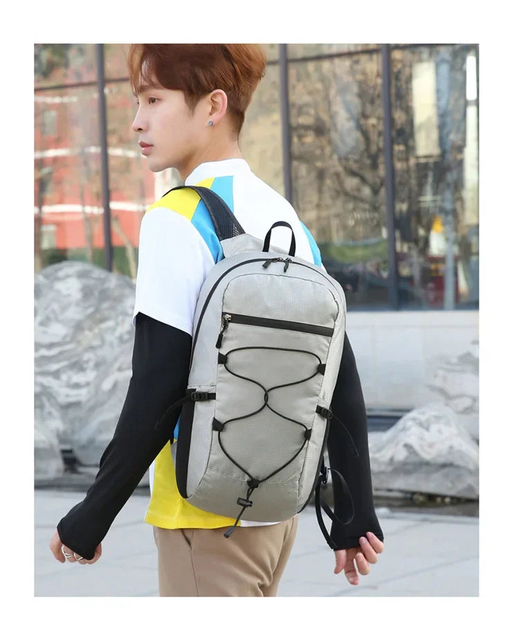 A young man wearing a white shirt and black sleeves is carrying a gray hiking backpack outdoors.
