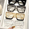 A display of four oversized rectangular reading glasses in black, leopard print, gold, and clear frames.