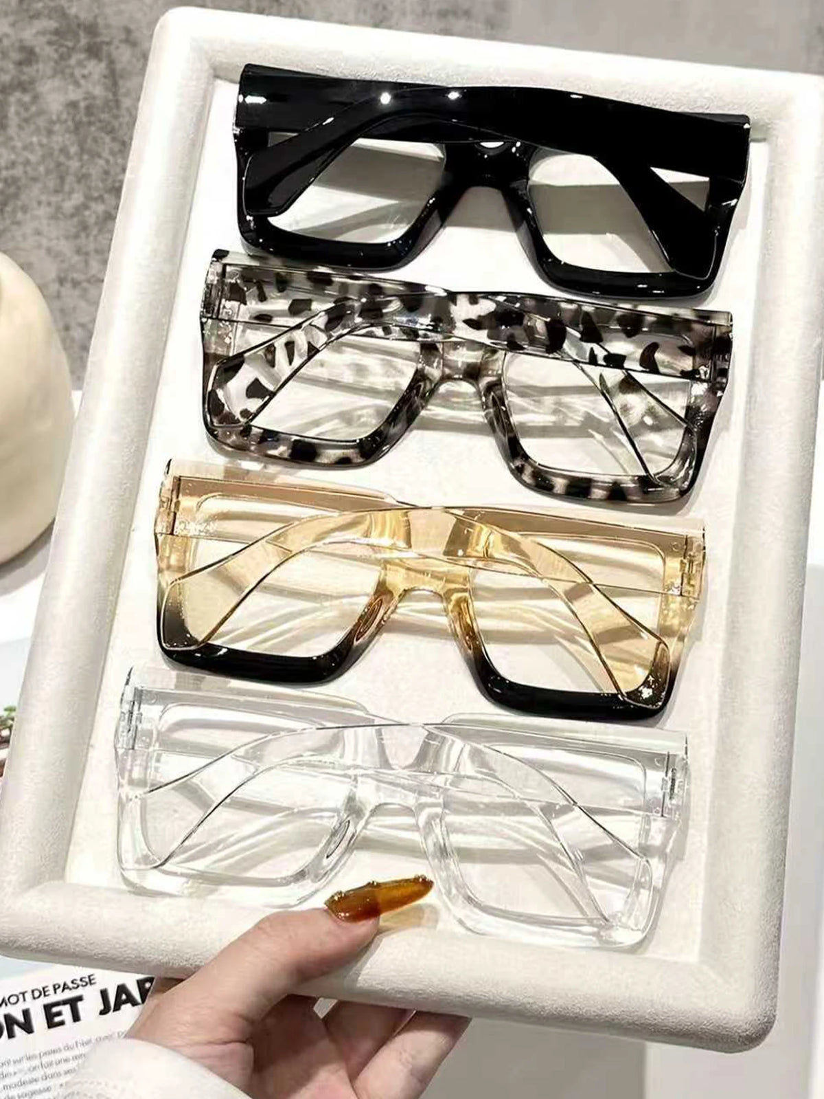 A display of four oversized rectangular reading glasses in black, leopard print, gold, and clear frames.