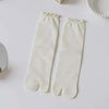 Pair of white knit crew socks with ruffle cuffs lying on a white surface.