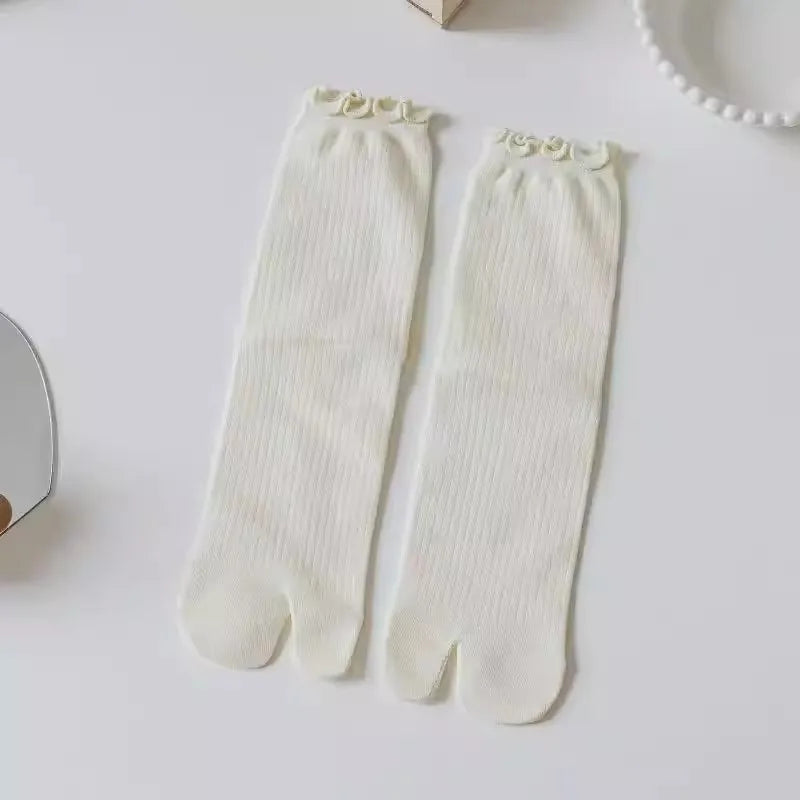 Pair of white knit crew socks with ruffle cuffs lying on a white surface.
