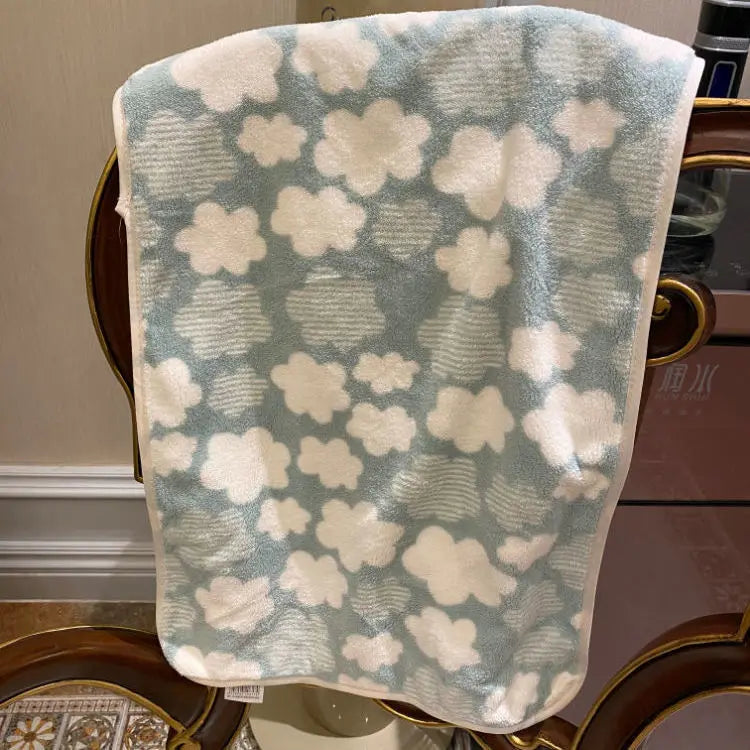 A soft coral fleece face towel with a light blue background and white floral pattern is displayed on a wooden surface.