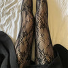 Black floral rattan fishnet hosiery worn on legs against a light background.
