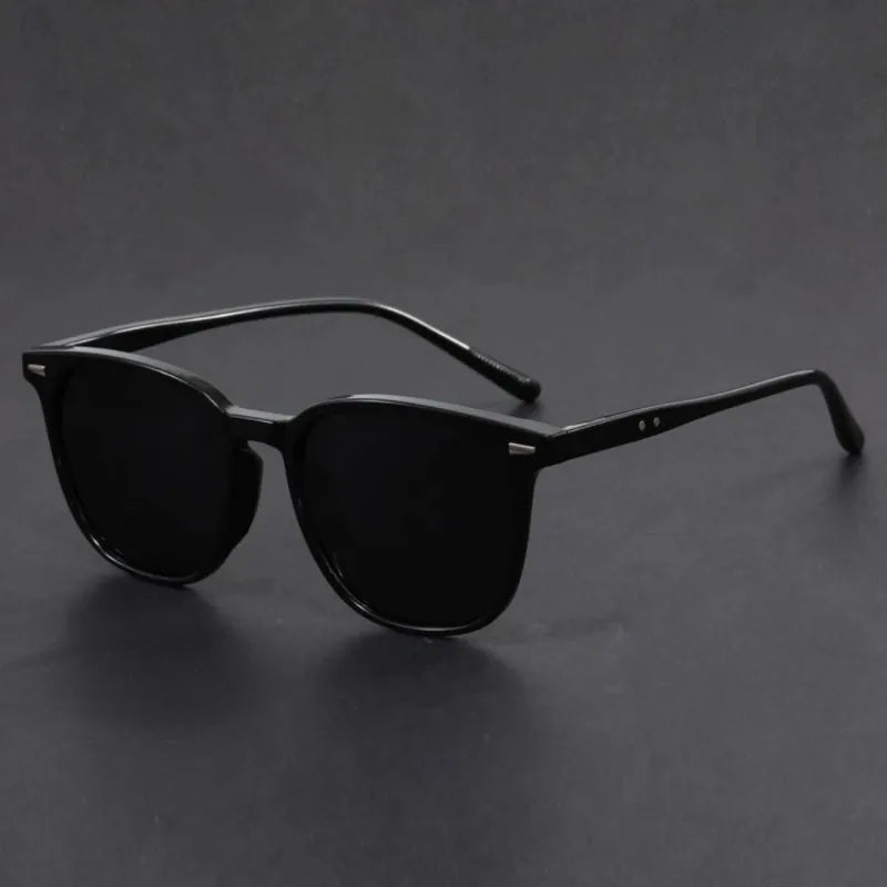 Black square sunglasses with thin arms resting on a dark surface.