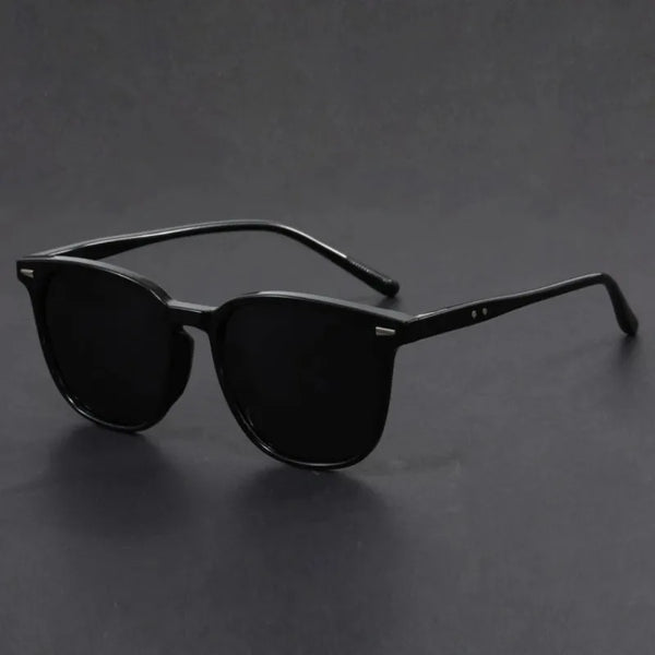 Gafas negras cuadradas con patillas finas sobre una superficie oscura.
